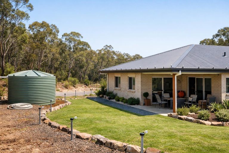 A suburban house beside bushland with visible preparedness features such as a water tank and tidy defendable space