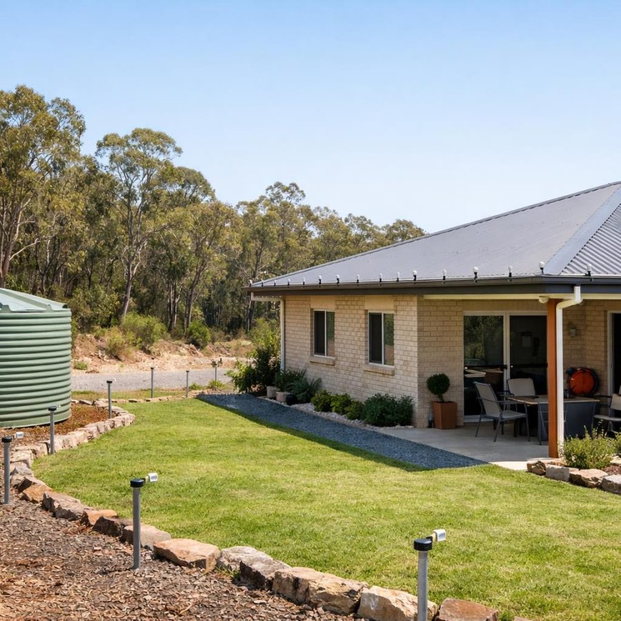 A suburban house beside bushland with visible preparedness features such as a water tank and tidy defendable space